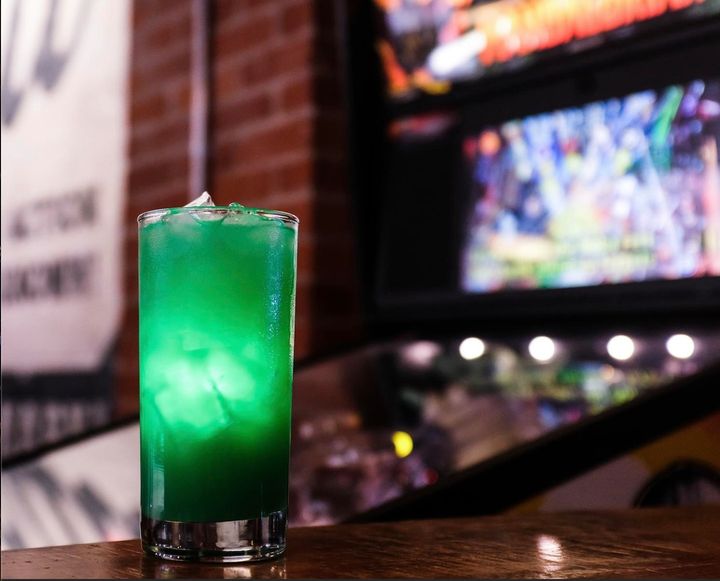 A shot of 16 Bit Bar's green Mandalorian cocktail in front of a vintage arcade game. Photo by Instagram user @16bitbar.