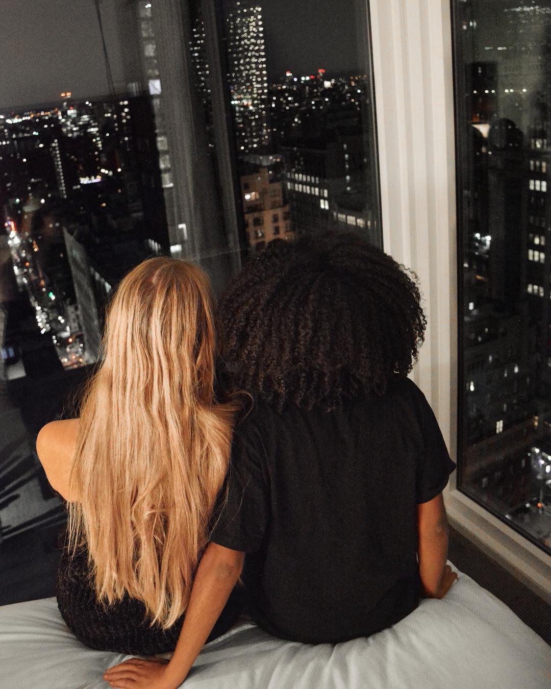 Couple Overlooking a City at Night from a Hotel Room. Photo by Instagram user @theangelinos_