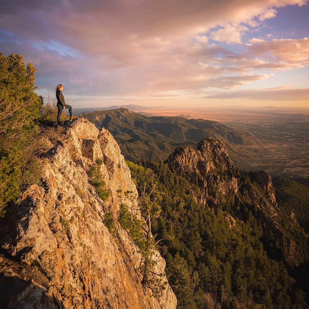 Woman looks down into a valley from the top of a mountain peak Photo by Instagram user @visitabq