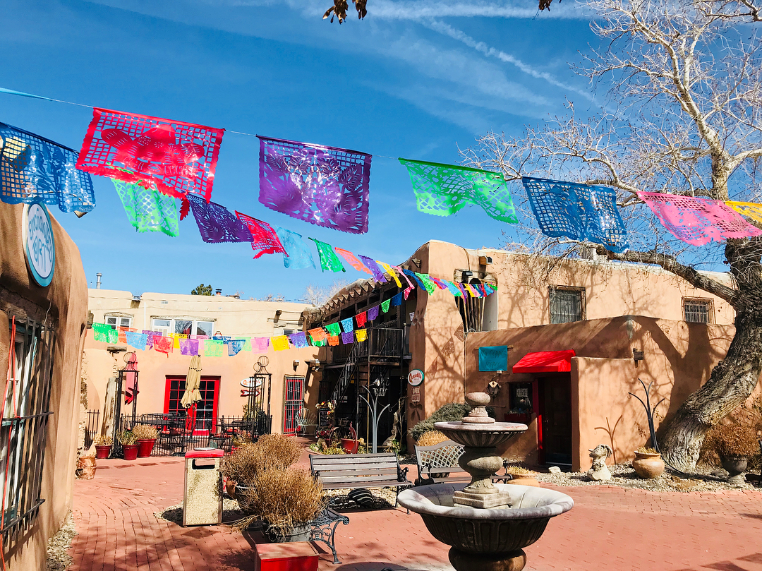 Courtyard adorned with colorful banners in Old Town Albuquerque. Photo by Instagram user @qhwinnie