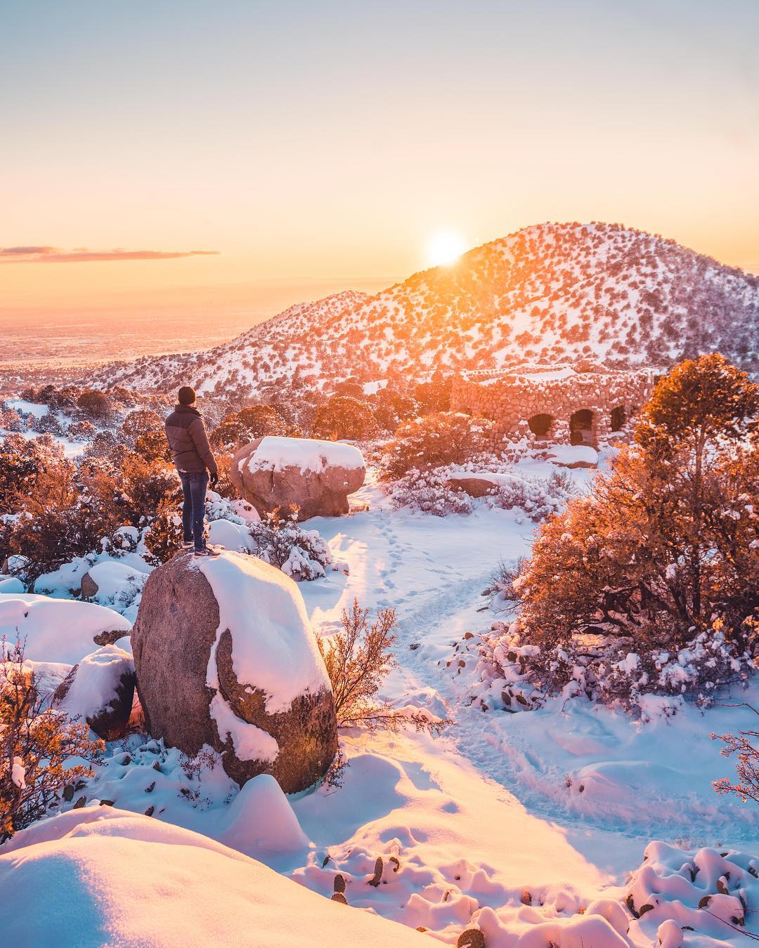 Man standing on a snow-covered rock looking at the horizon. Photo by Instagram user @bklyphoto