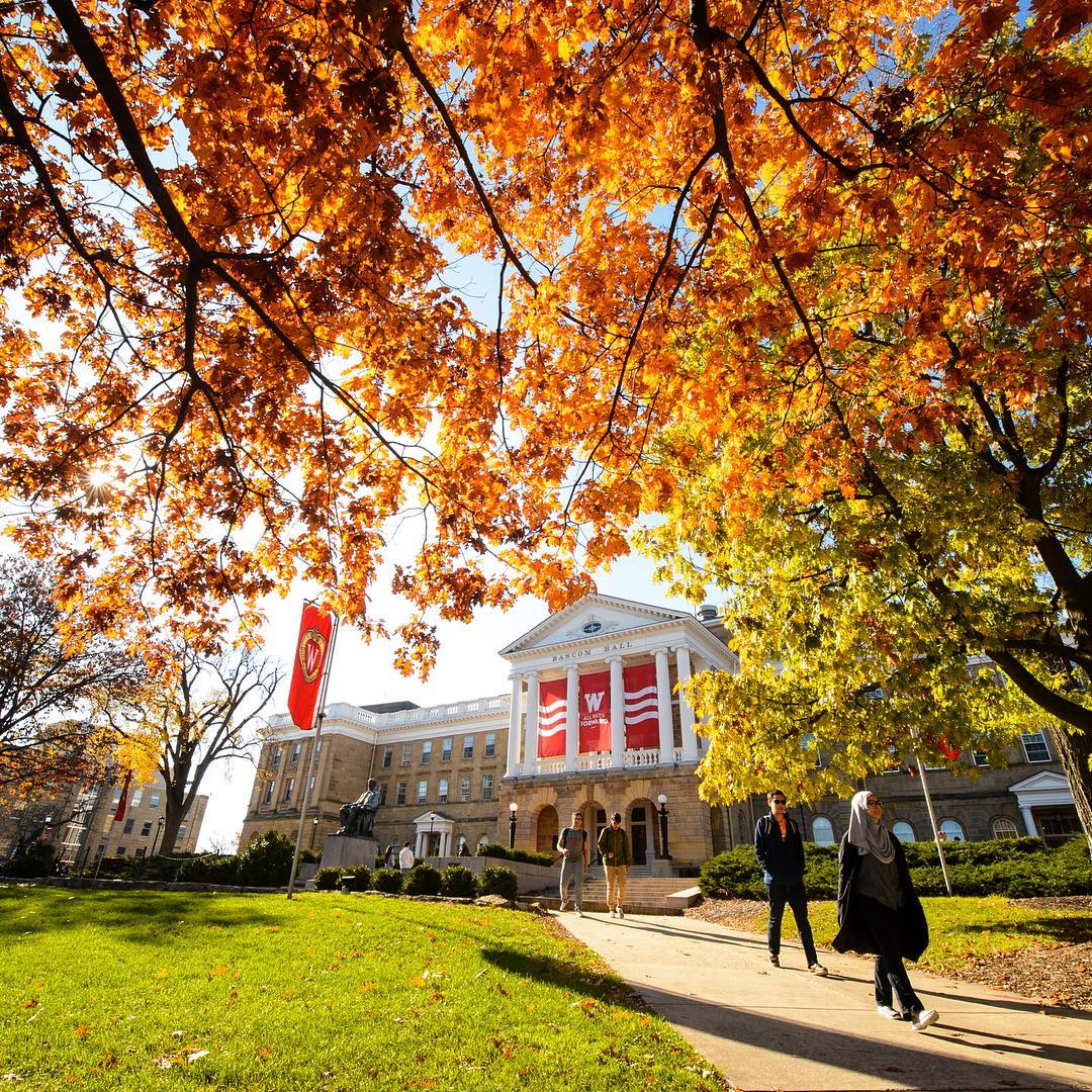 View of campus with students walking, trees with yellow leaves and a large building in the background. Photo by Instagram user @uwmadison