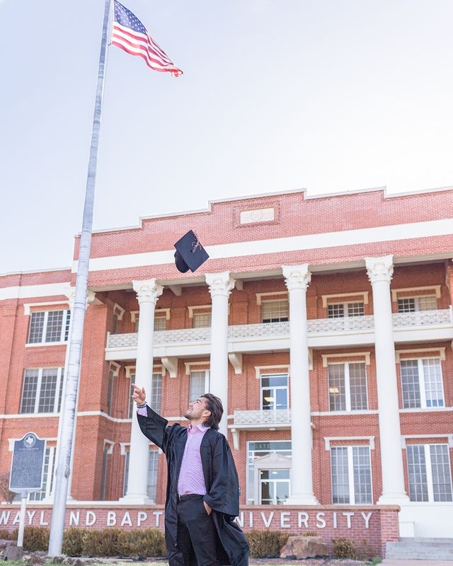 A graduating student throwing their cap in front of Wayland Baptist University. 