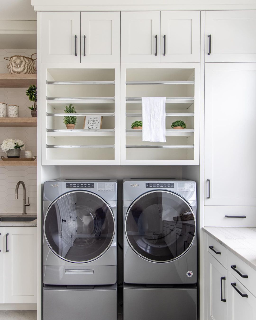 White laundry room with side-by-side washer and dryer unit below drying racks. Photo by Instagram user @kimberlyparkerdesign