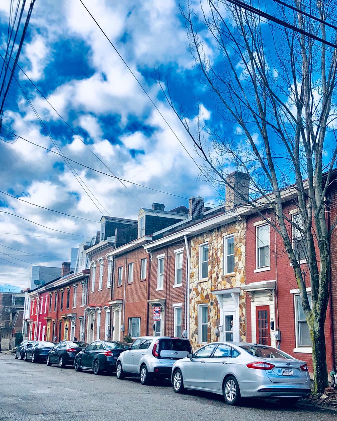 Red, yellow and white townhomes line the street stacked side by side with cars parked outside. Photo by Instagram user @shelbiemoser