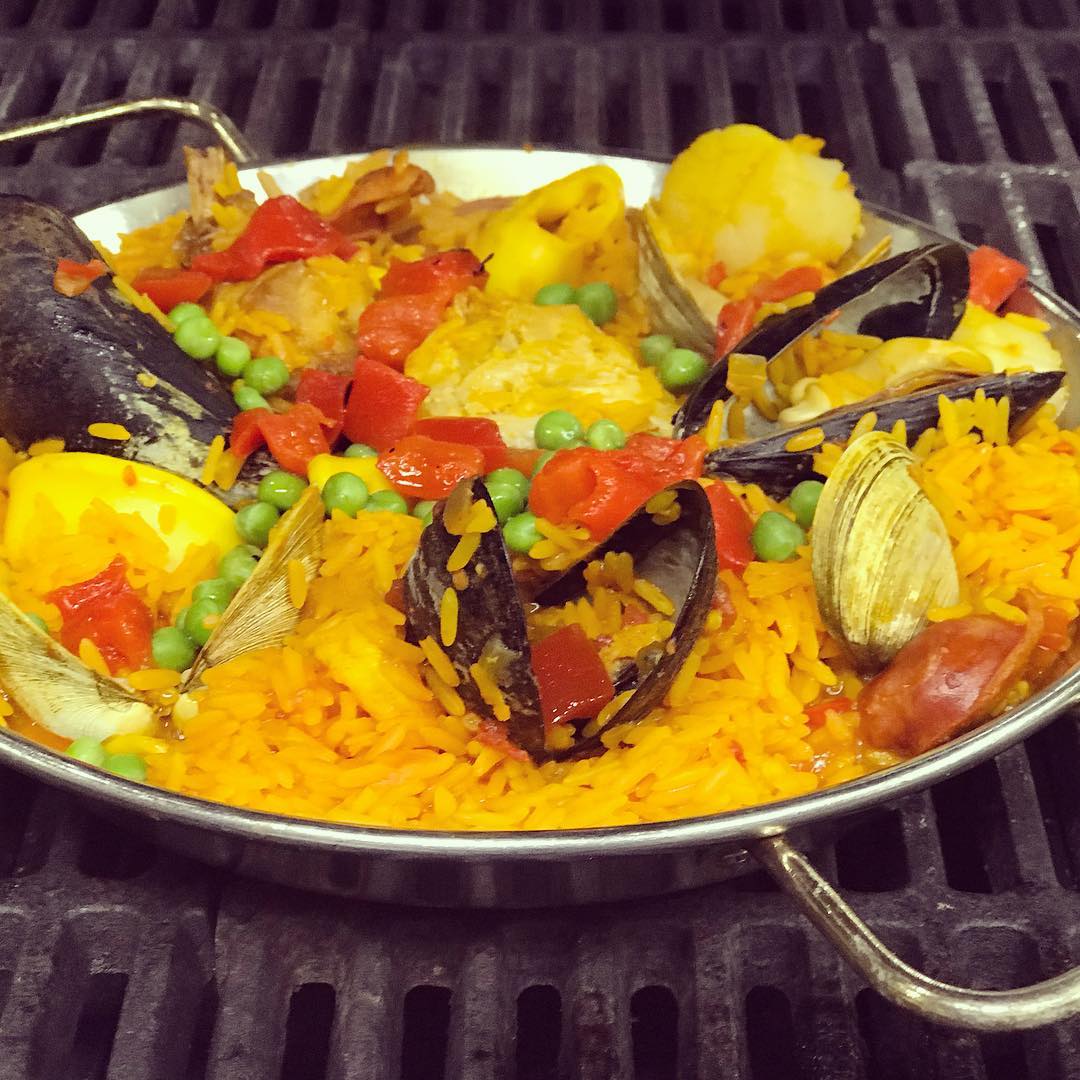 Closeup of pan of paella cooking on a grilltop. Photo by Instagram user @fornos_of_spain