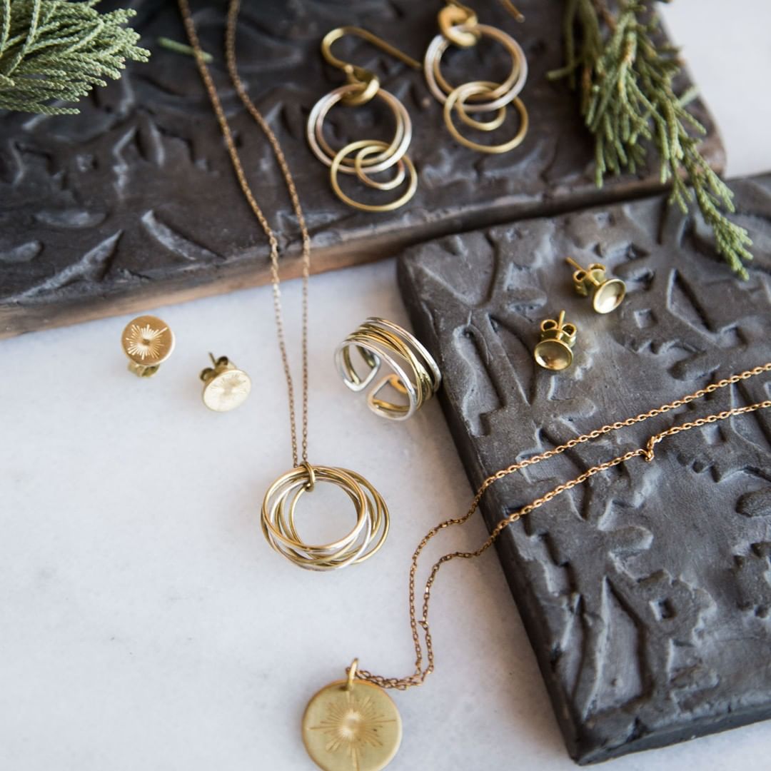 Gold necklaces and gold earrings on black stone. Photo by Instagram user @tenthousandvillages