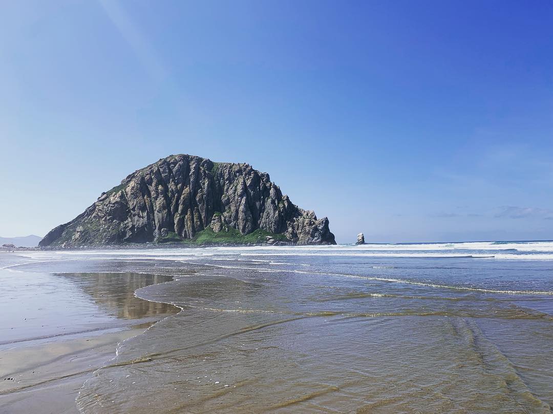 Dark rock formation in the middle of water in Morro Bay. Photo by Instagram user @carebearcarito
