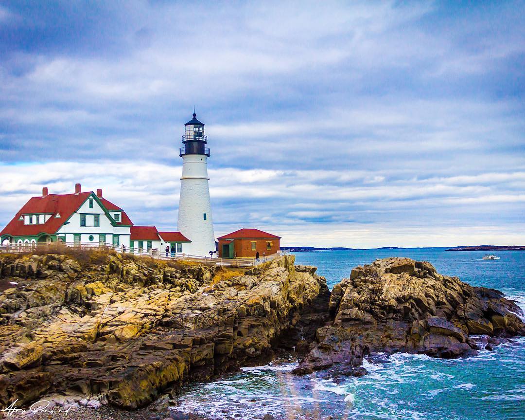 White lighthouse on rocks next to water in Portland, Maine. Photo by Instagram user @_absolutphotography