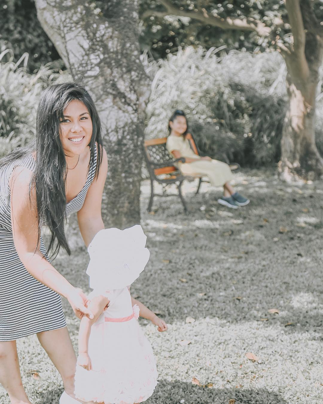 Dark-haired woman holding little girl in the park. Photo by Instagram user @lovealwayscatherine