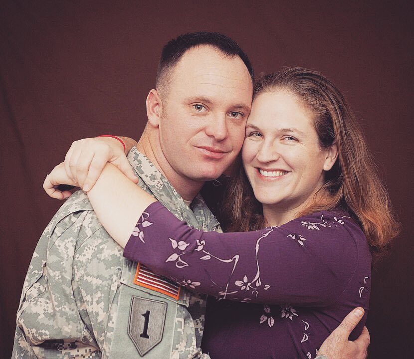 Military husband hugging his wife in front of purple backdrop. Photo by Instagram user @soldierswifecrazylife
