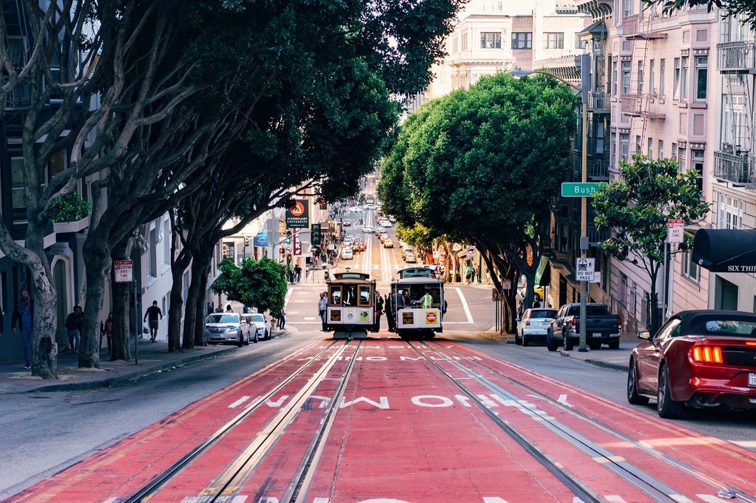 Two San Francisco trolleys riding on tracks down a tree-lined street. Photo by Instagram user @hyattregencysf_soma