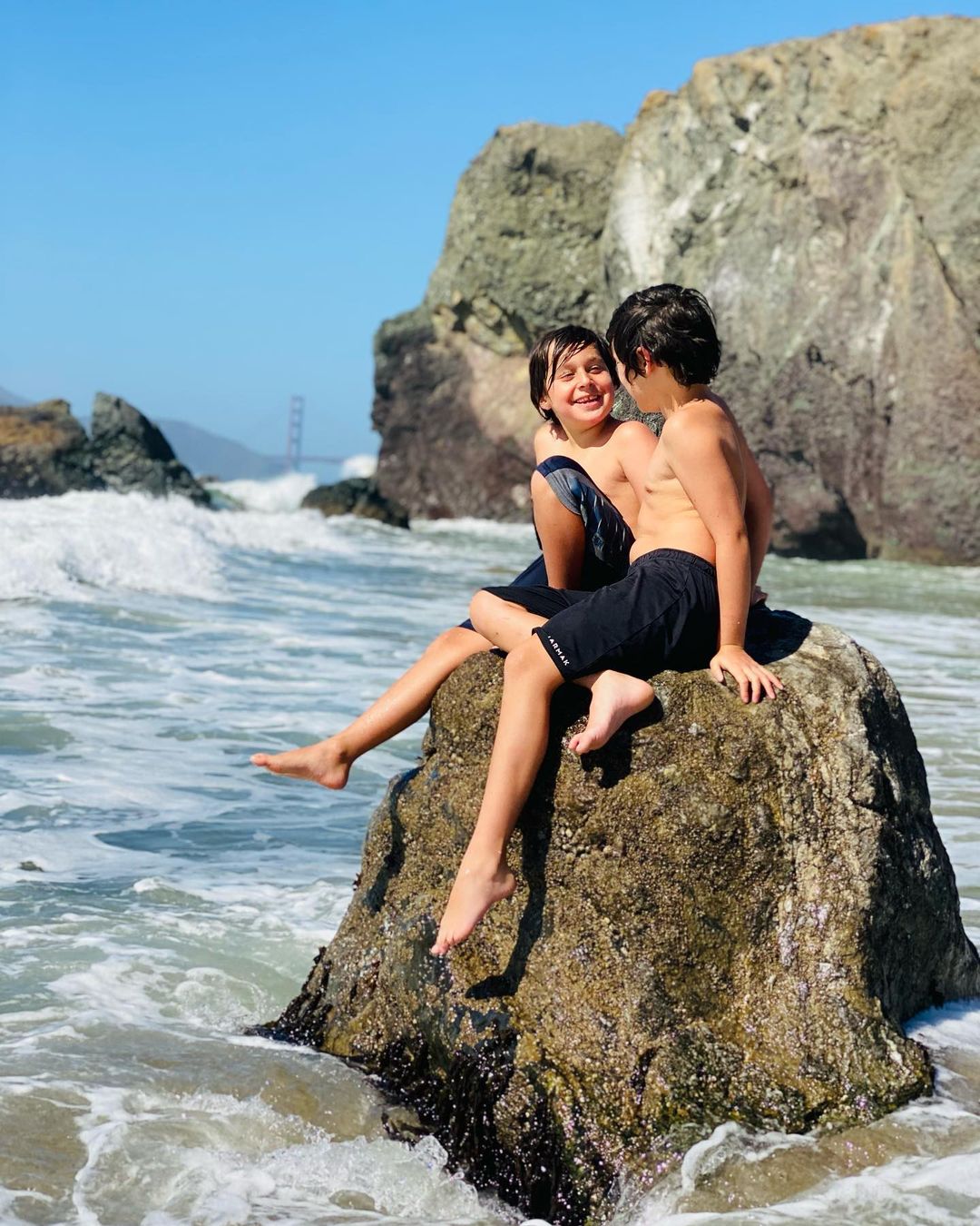 Two kids sitting on a rock on a San Francisco beach. Photo by Instagram user @valentinaorantes