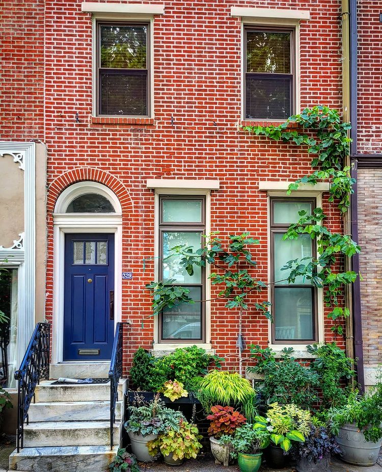 Brick home exterior with blue door, white trim, and potted plants. Photo by Instagram user @jeffreydwright