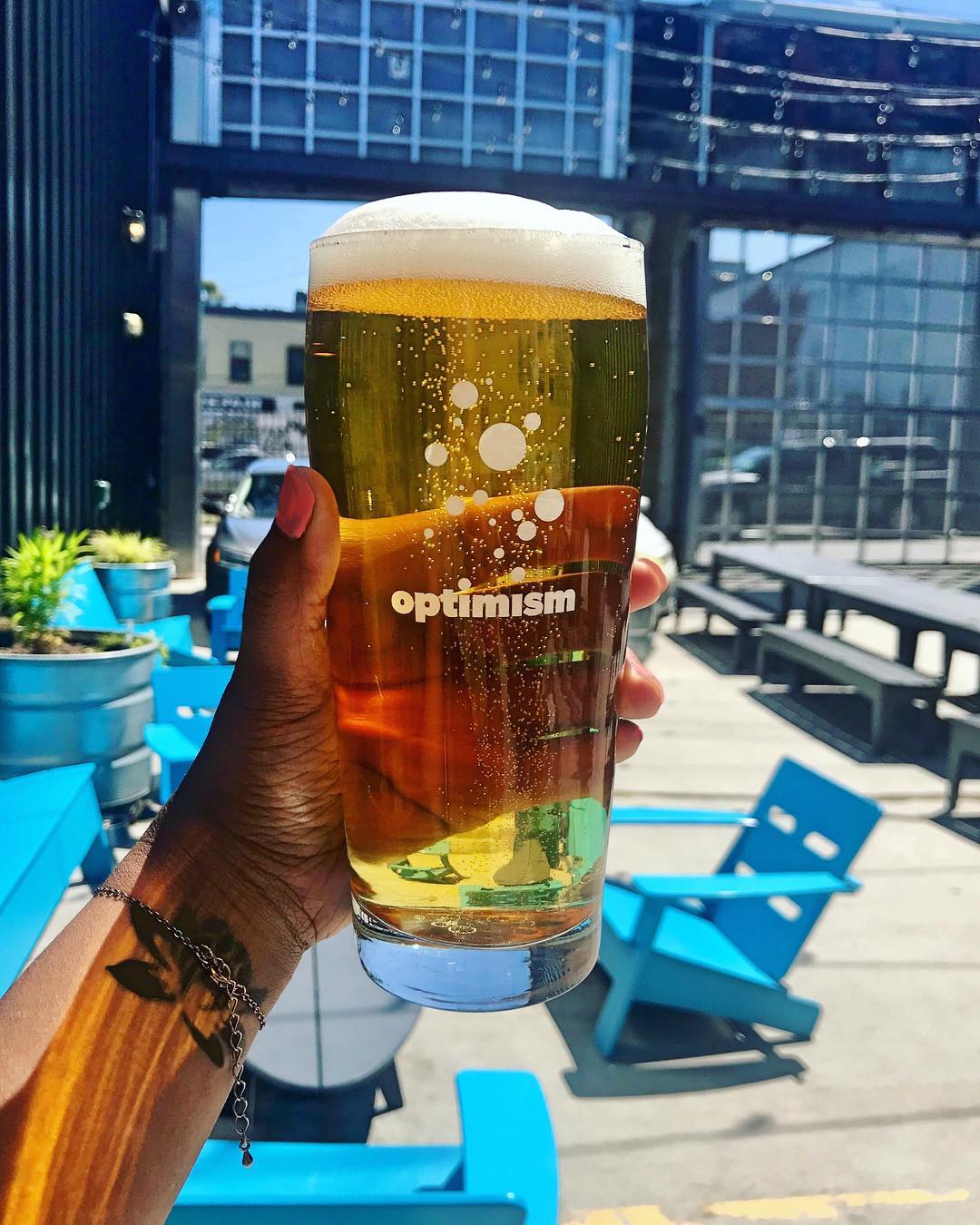 A hand holding a glass of beer from Optimism brewing. Photo by Instagram user @optimismbrewing