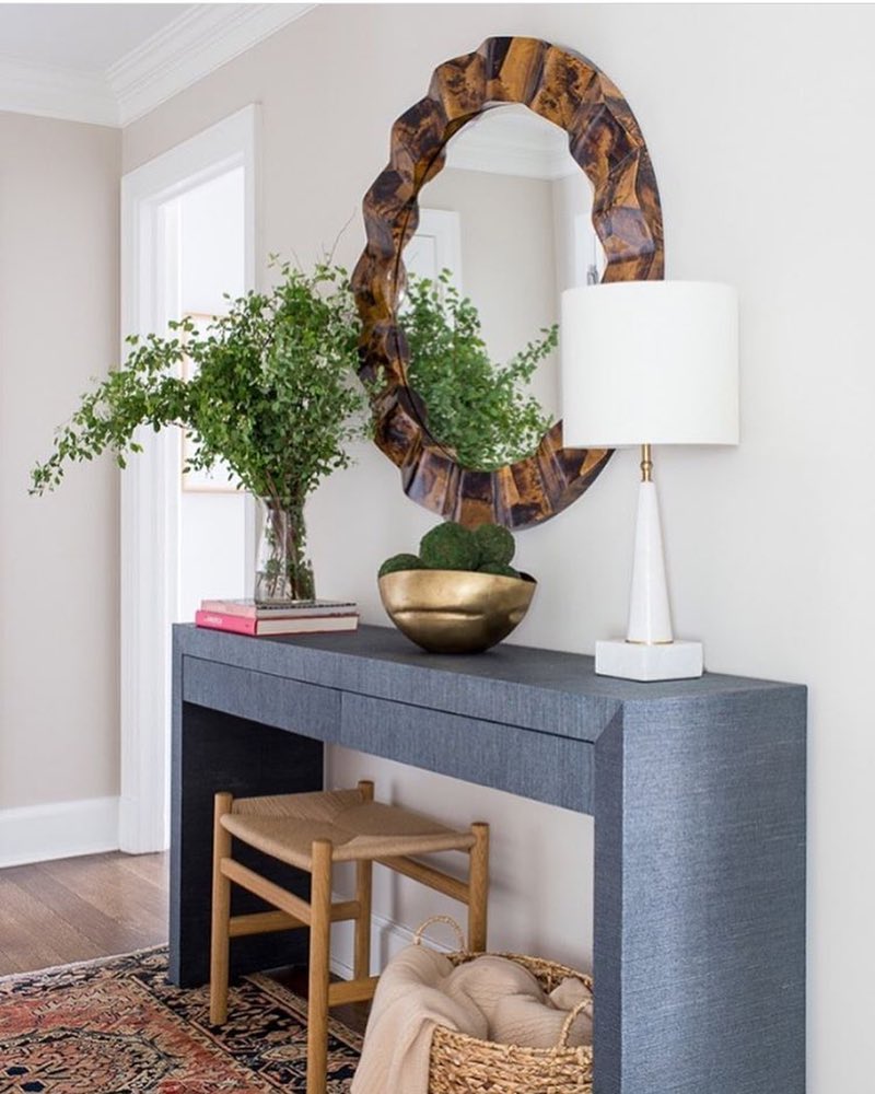 Round wood mirror above gray table in hallway with lamp and plant on top of it. Photo by Instagram user @livenupdesigns