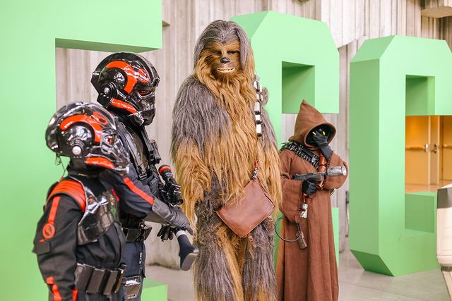A group of four cosplayers in Star Wars-themed costumes. The Chewbacca cosplayer is looking into the camera.