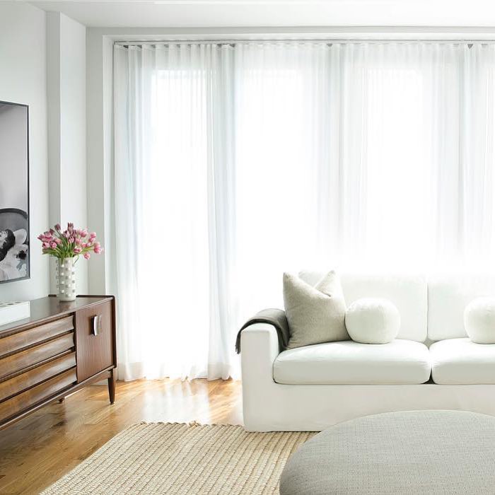 Living room with white curtain and a white comfy couch. Photo by Instagram user @carawoodhouseinteriors
