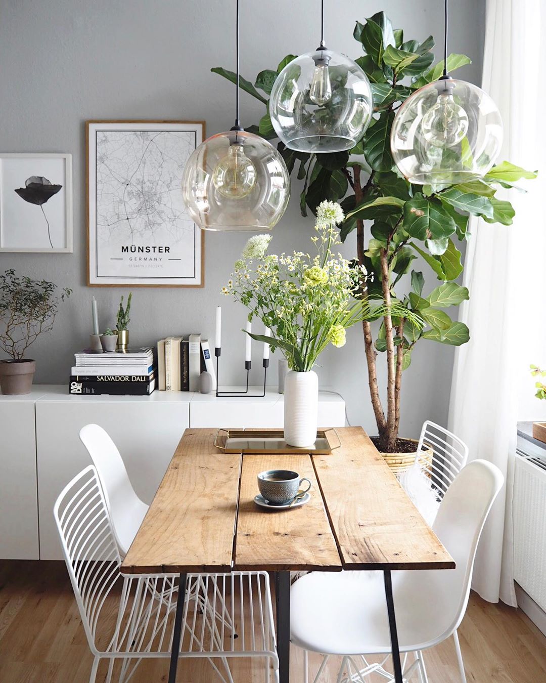 White dining room with wood table and tree in the corner designed by Scandinavian style. Photo by Instagram user @oursweetliving