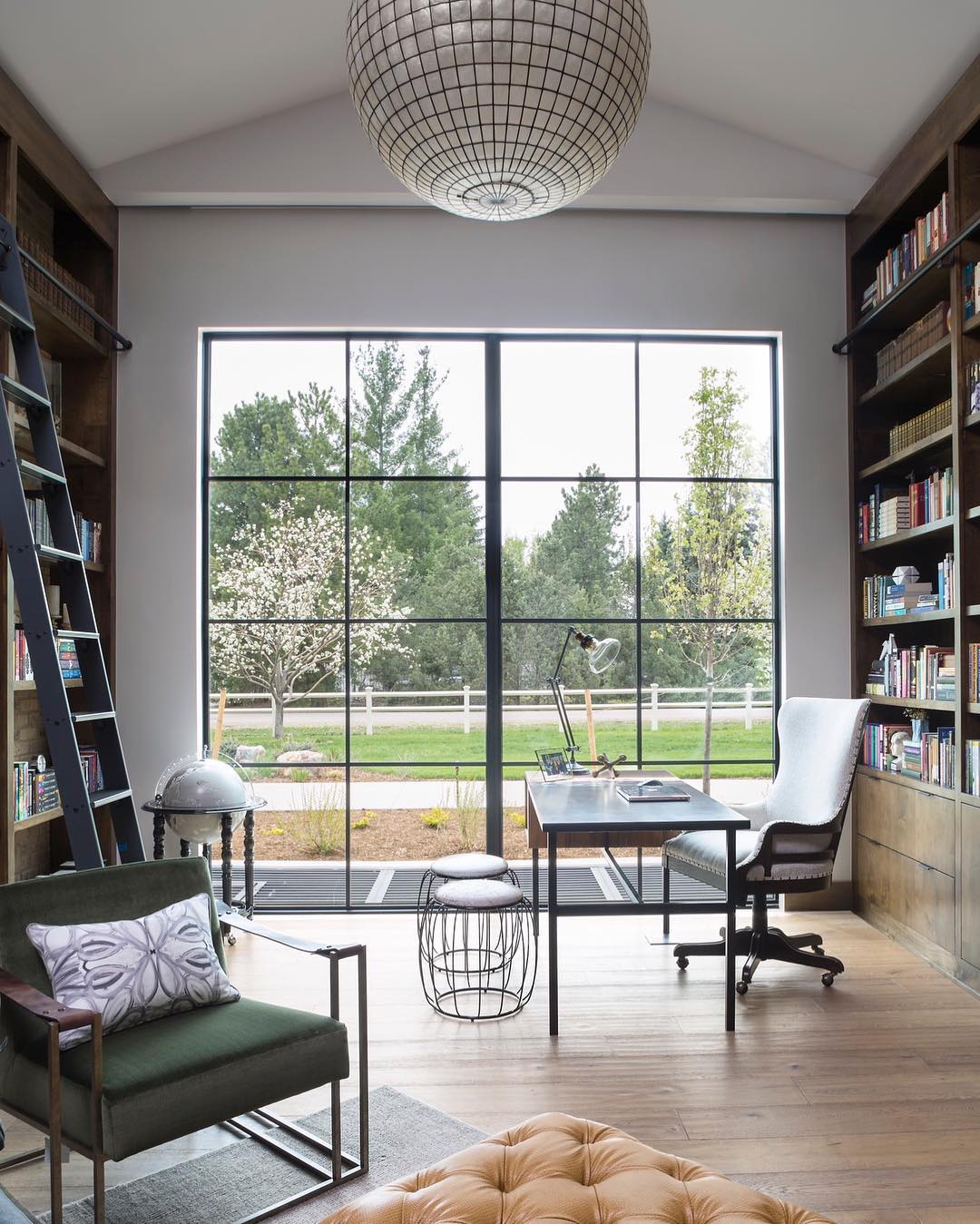 Home office with big windows and large bookcases and wire stools. Photo by Instagram user @duetdesigngroup