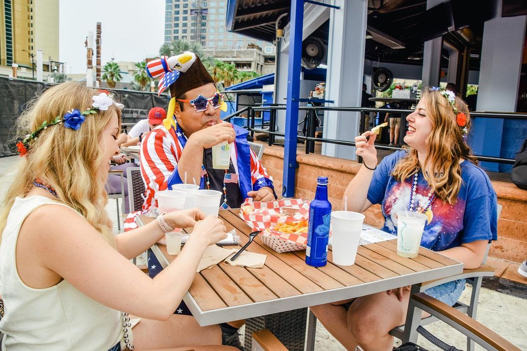 Three friends enjoying food and drinks on an outdoor patio. Photo by Instagram user @thesailtampa