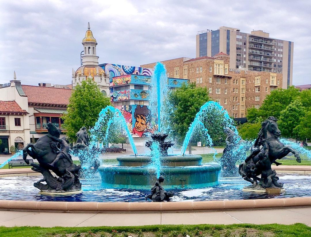 A water fountain wirh its water dyed blue and with several statues such as men riding horses and children with sea animals. @kcmoparks