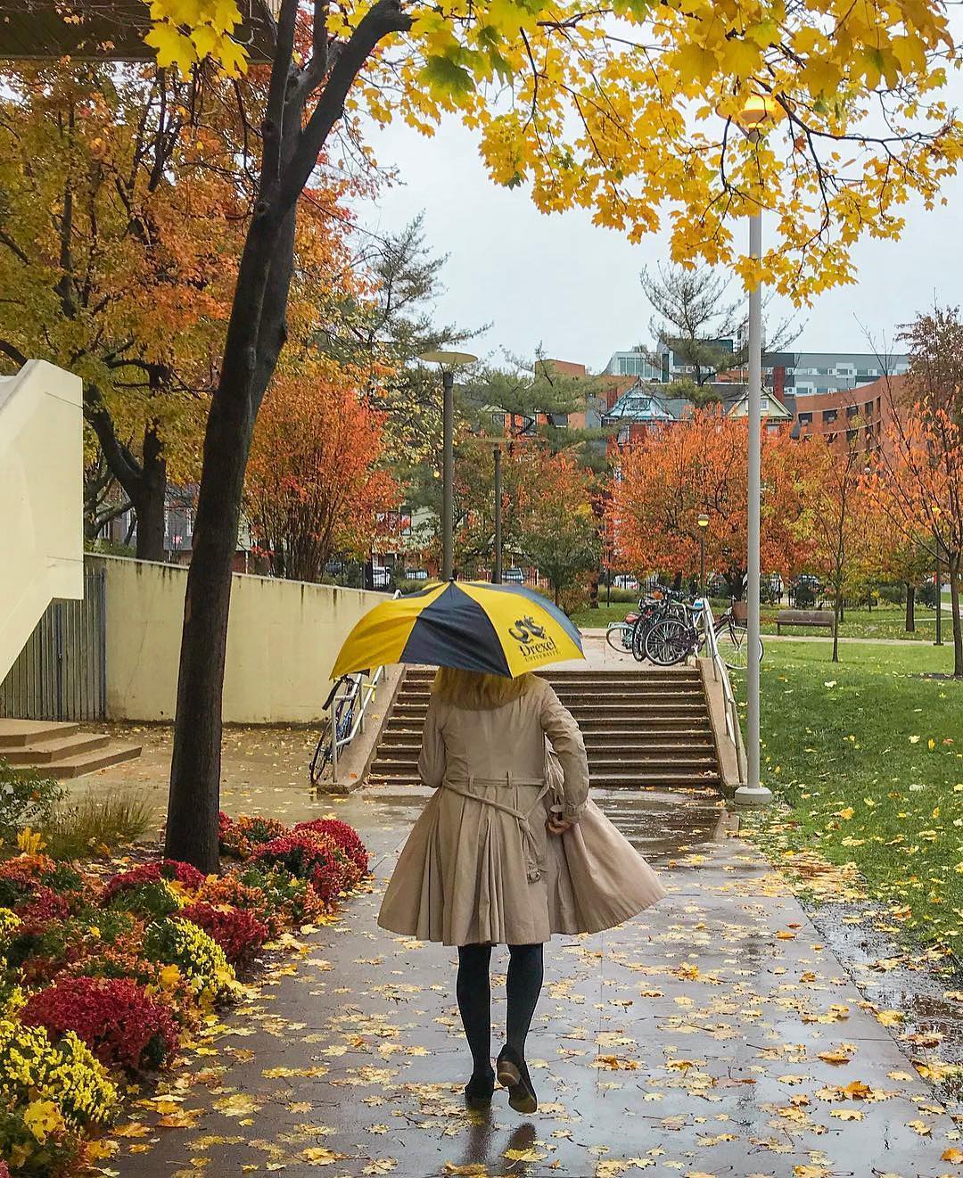 Girl walking on a college campus with an umbrella. Photo by Instagram user @pavlosmixalis