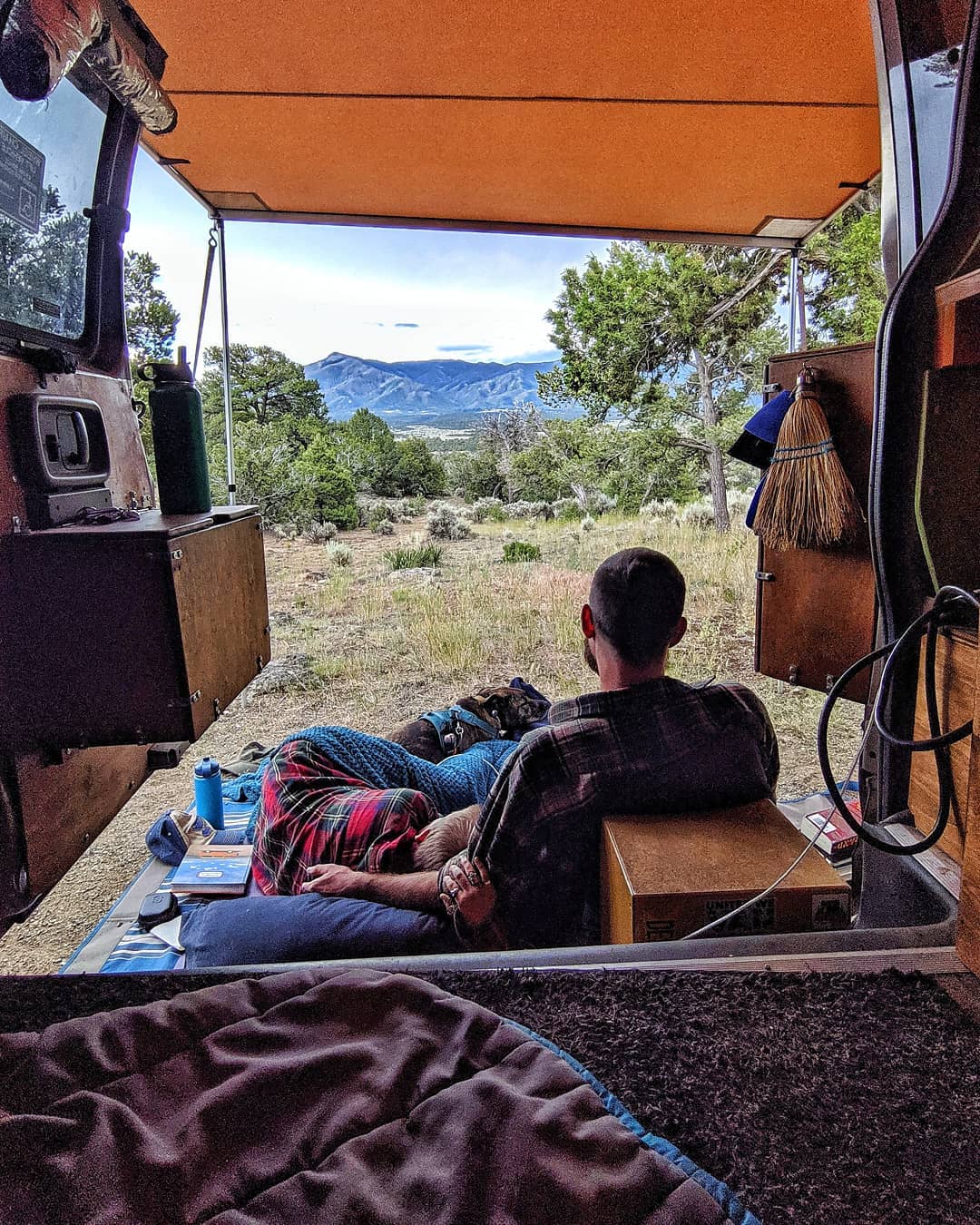 Couple sitting on the back of their van looking out at the mountains. Photo by Instagram user @gnomad_home