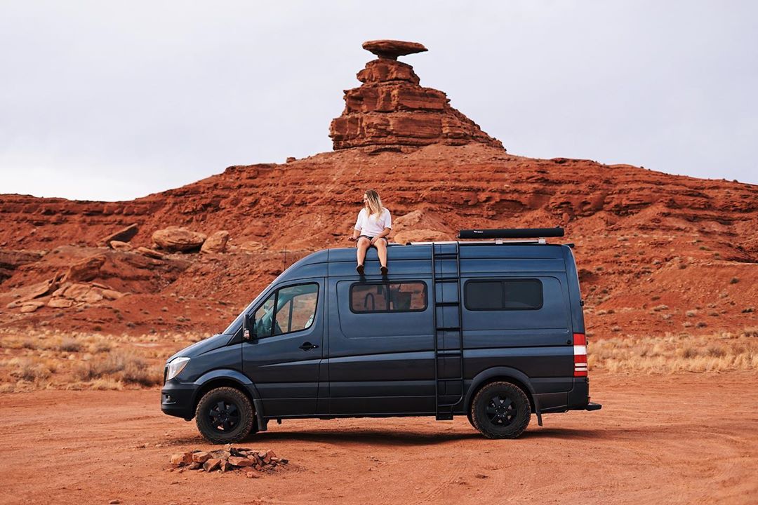 Girl sitting on the top of a van in the desert. Photo by Instagram user @soweboughtavan