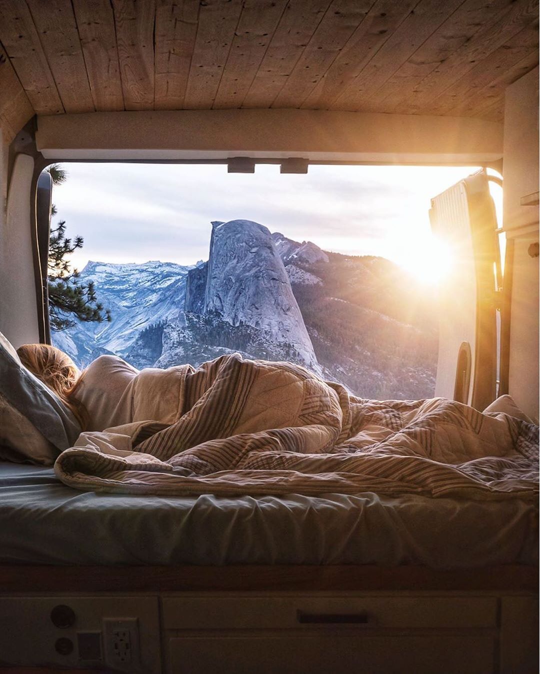 Girl laying in her van looking out the back at the mountains. Photo by Instagram user @jess.wandering