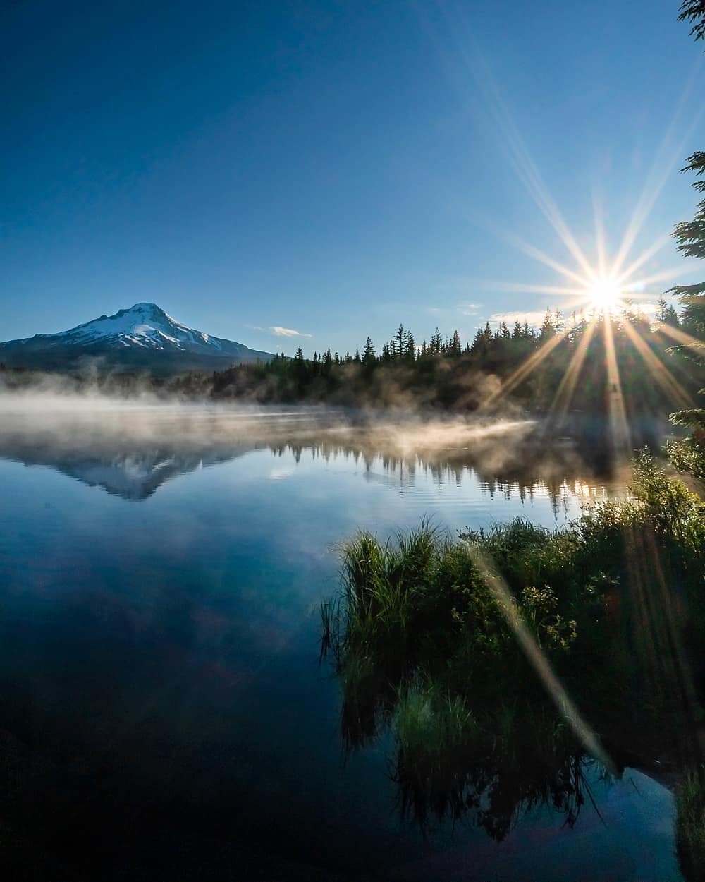 Sun shining over crystal clear lake with mountains in the back at Mt Hood National Forest, OR. Photo by Instagram user @browneyedsmile808