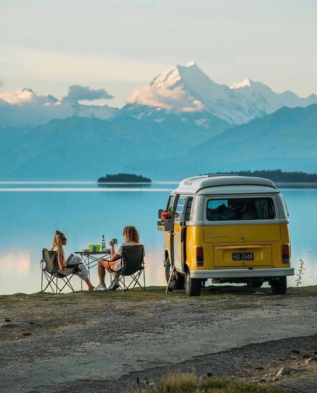 Two people sitting in chairs outside of their yellow van by the mountains. Photo by Instagram user @vanlife.living