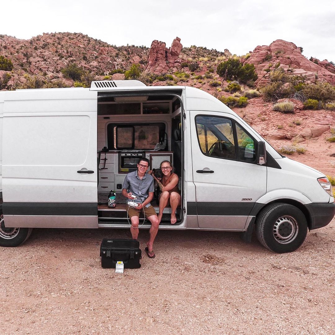 Couple sitting out of the side of their white sprinter van. Photo by Instagram user @simplholistic