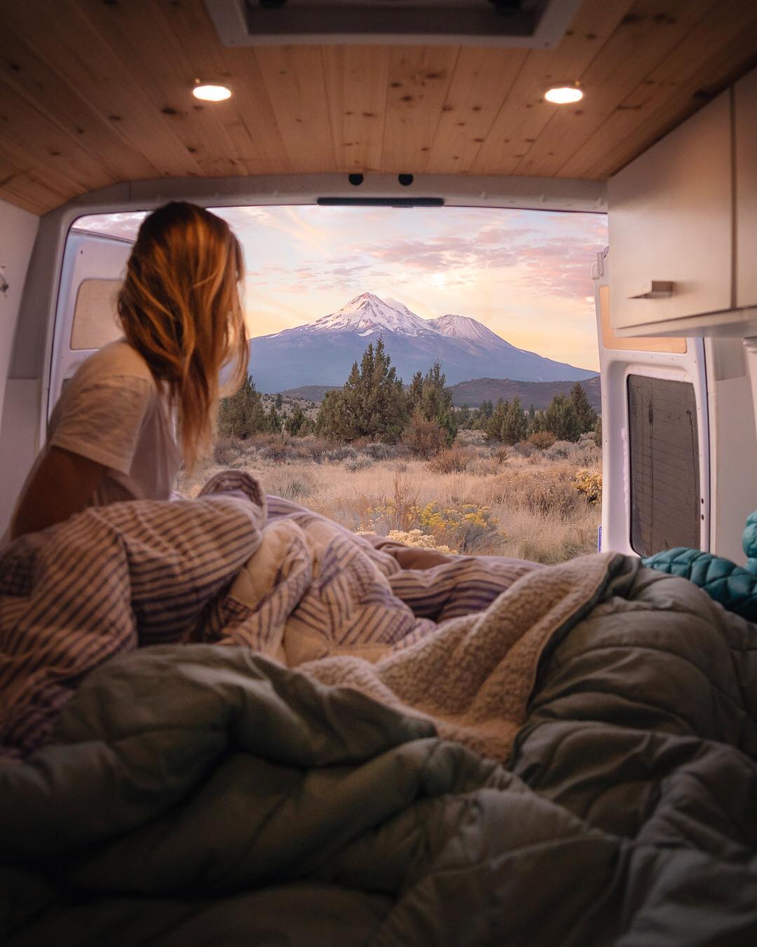 Girl sitting in the back of a van looking at the mountains. Photo by Instagram user @jess.wandering