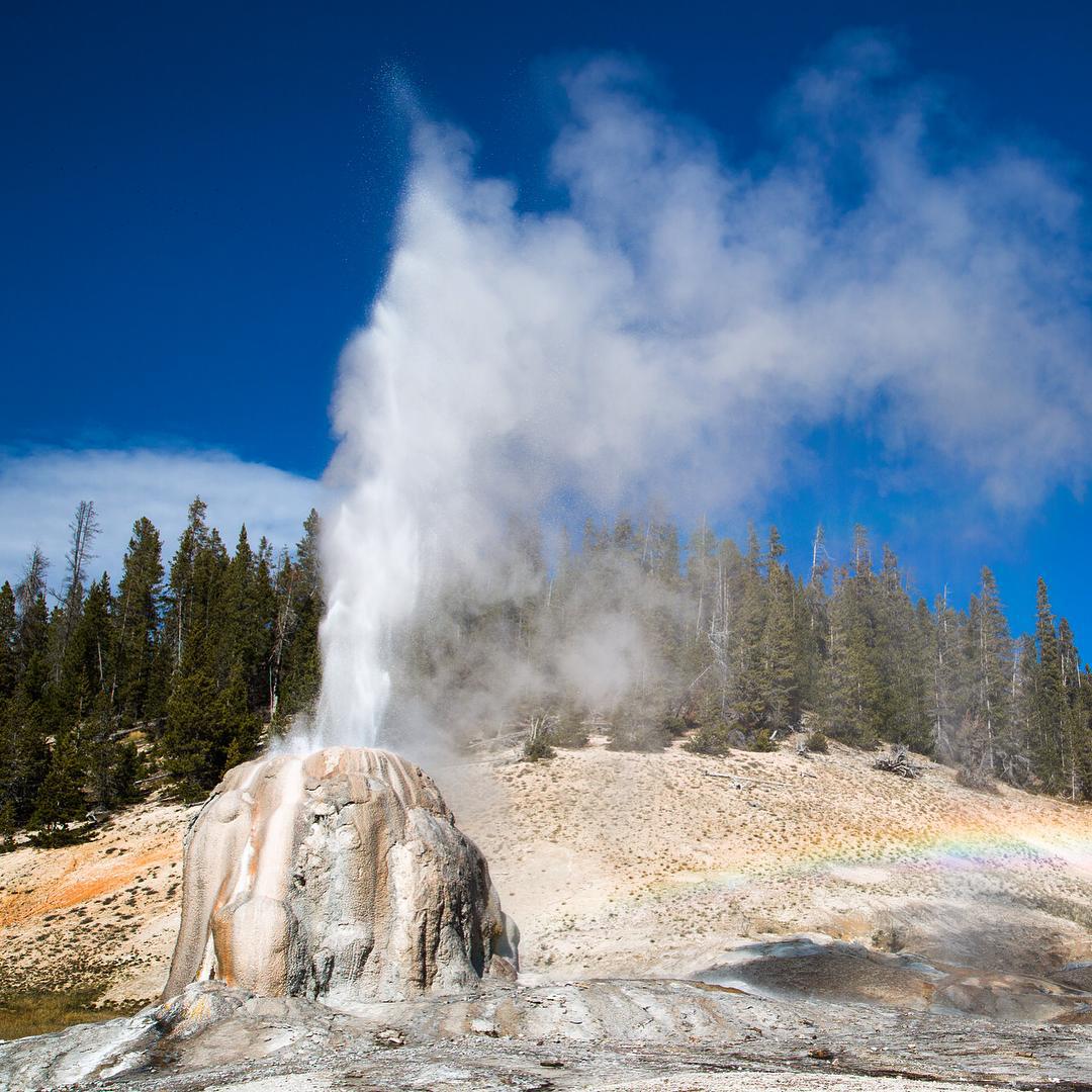 Geyser shooting out of the ground on a sunny day at Yellowstone National Park, WY. Photo by Instagram user @yellowstonenps