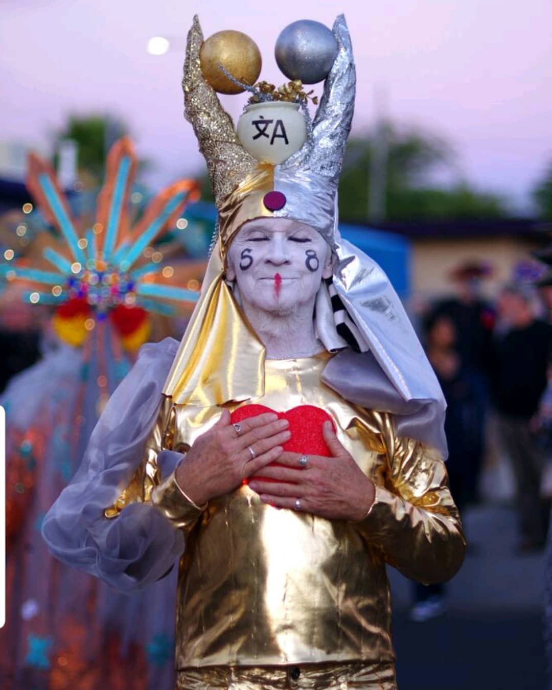 Man dressed in white and gold holding a heart for a festival. Photo by Instagram user @allsoulsprocessiontucson