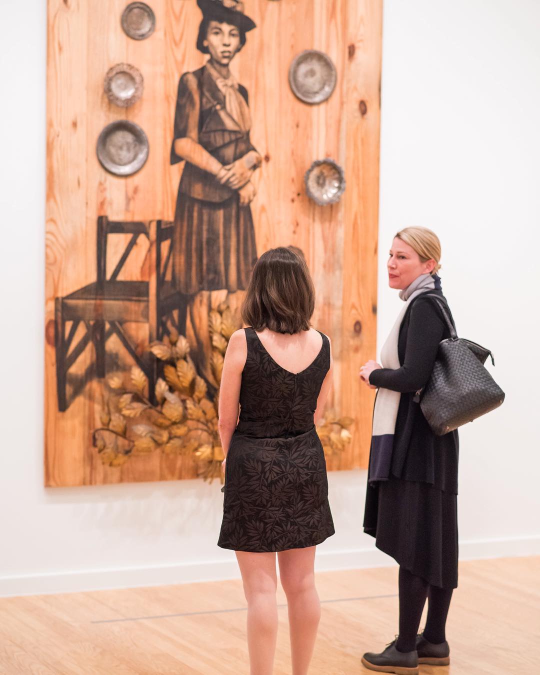 Two women looking at a wood painting. Photo by Instagram user @bhammuseum
