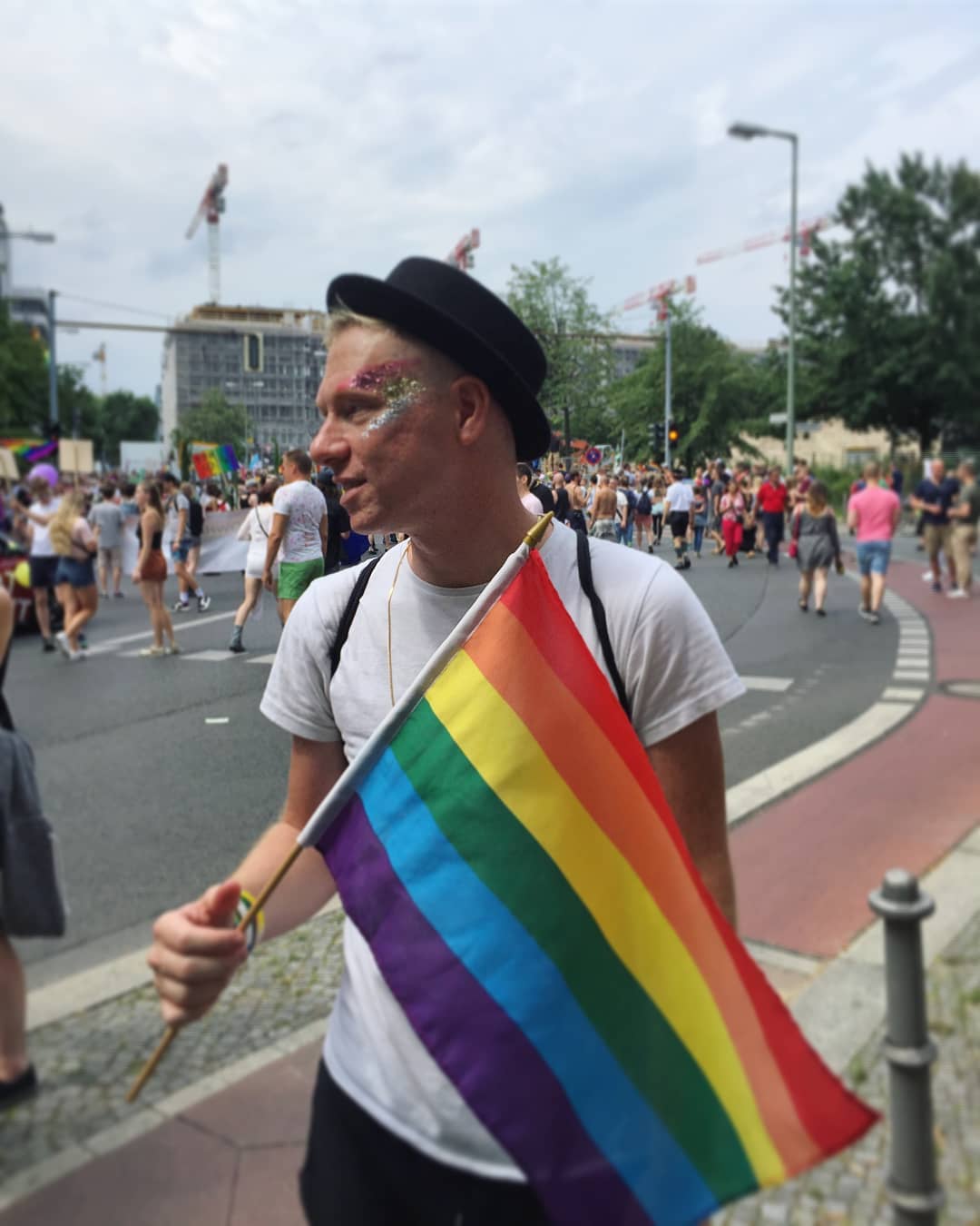 Guy wearing glitter and holding a rainbow flag. Photo by Instagram user @travelsofadam