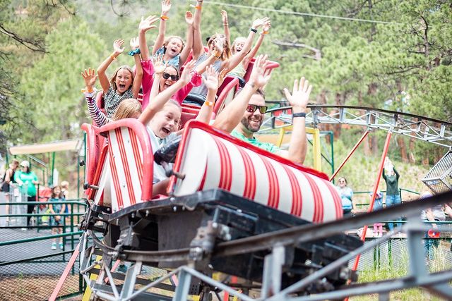A full roller coasterthat is candy cane striped, with the riders waving their hands in the air as they turn a corner on the ride. @northpolecolorado