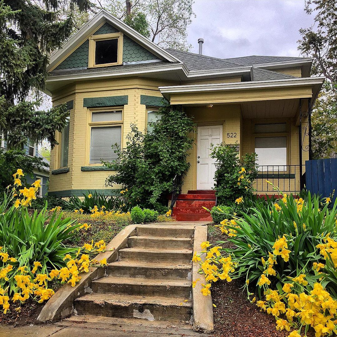 Yellow house with green trim and yellow flowers in the front yard. Photo by Instagram user @lovelyoldhomes