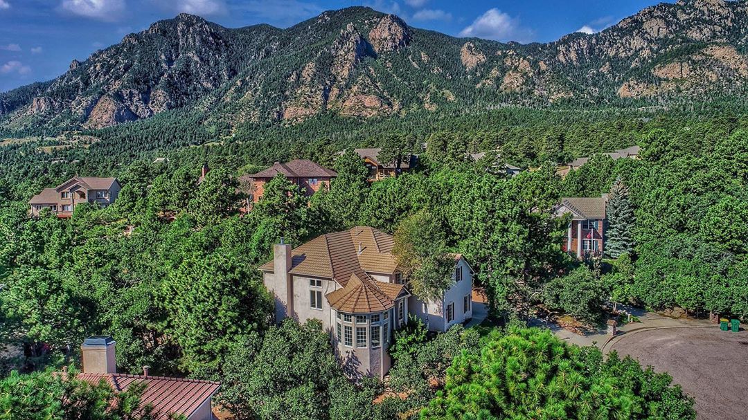 A brown home surrounded by trees and mountains. Photo by Instagram user @coloradosprings.homes