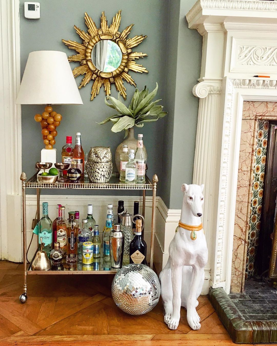 Bar cart with bottles on it and a white dog statue. Photo by Instagram user @thevintagetraderuk