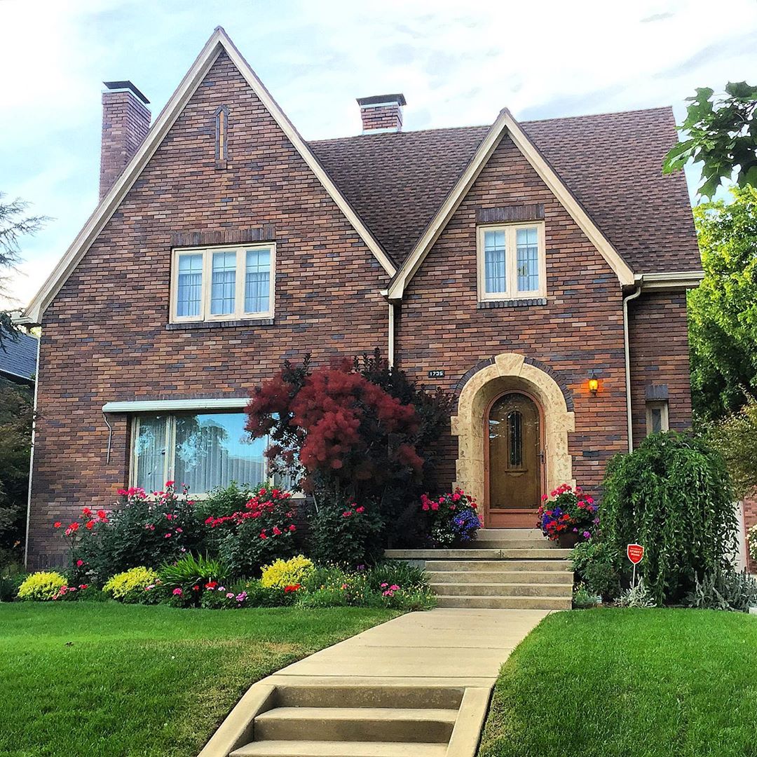 Red brick house with tan trim and flower hedges. Photo by Instagram user @lovelyoldhomes