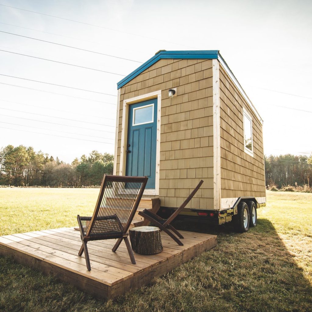 brown tiny home with blue roof and two patio chairs photo via @be_settled