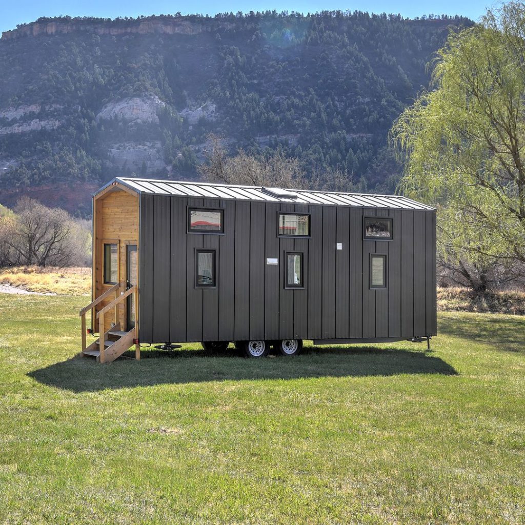 Brown tiny home with mountain background and green grass photo via @escalantevillage