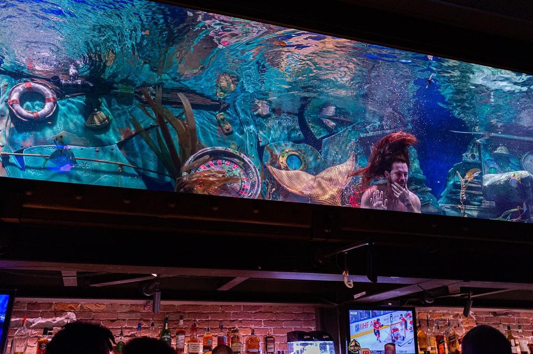 A mermaid in the Dive Bar looking out of the water tank. Photo by Instagram user @ghlsh8.