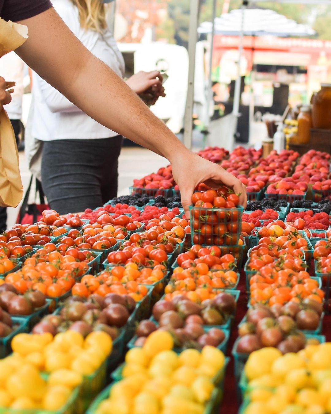 Person grabbing a container of cherry tomatoes at the Midtown Farmers Market in Sacramento. Photo by Instagram user @midtownfarmersmarket