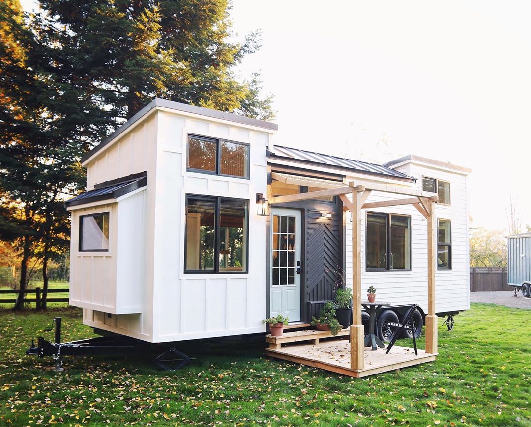 White tiny home with black doors and porch. Photo by Instagram user @handcraftedmovement