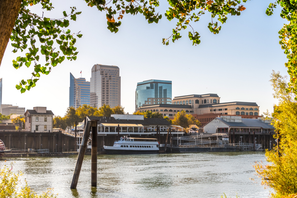 Skyline view of Sacramento with a body of water in front of it, framed by trees.