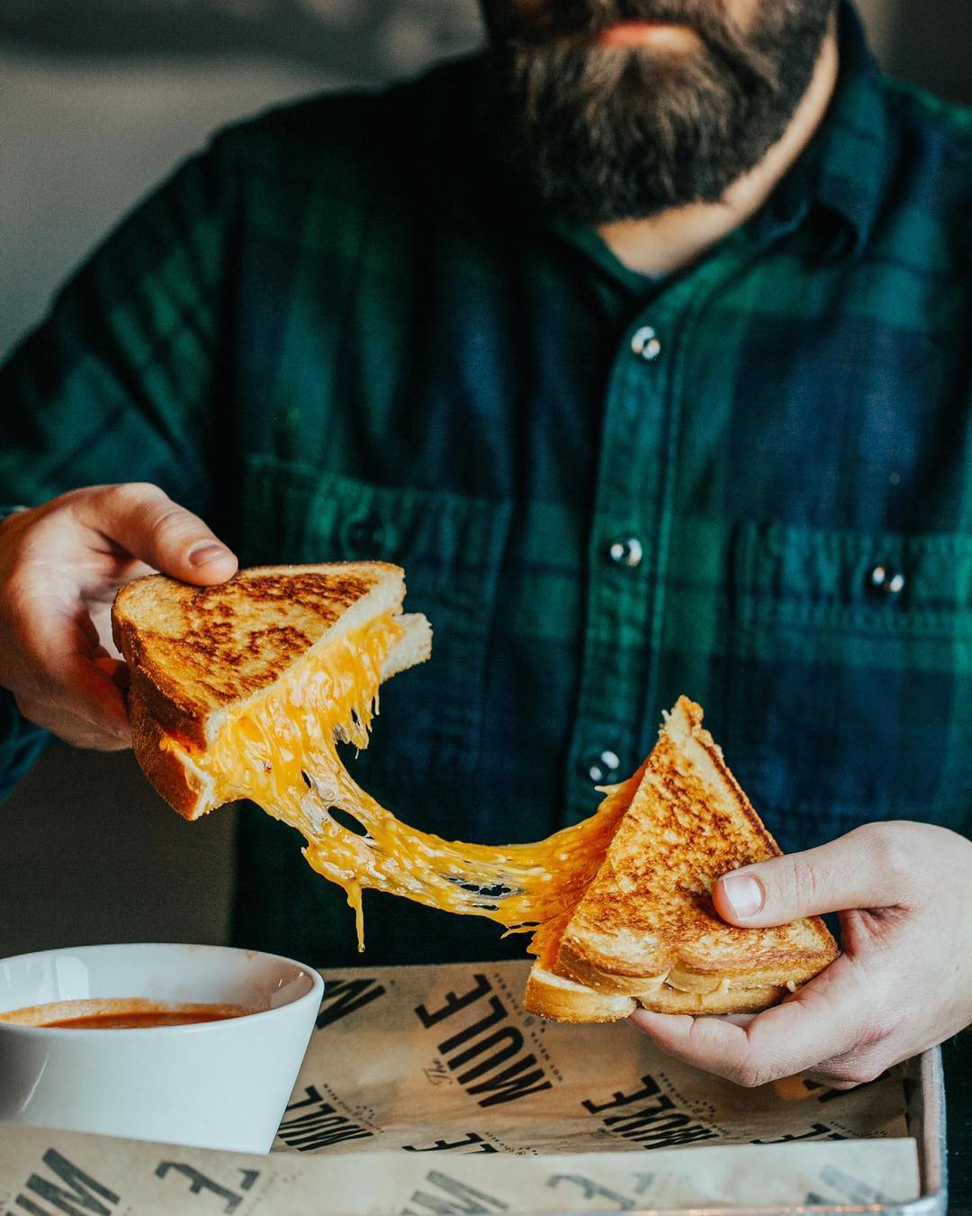 Guy pulling apart cheesy grilled cheese. Photo by Instagram user @dwellingtable